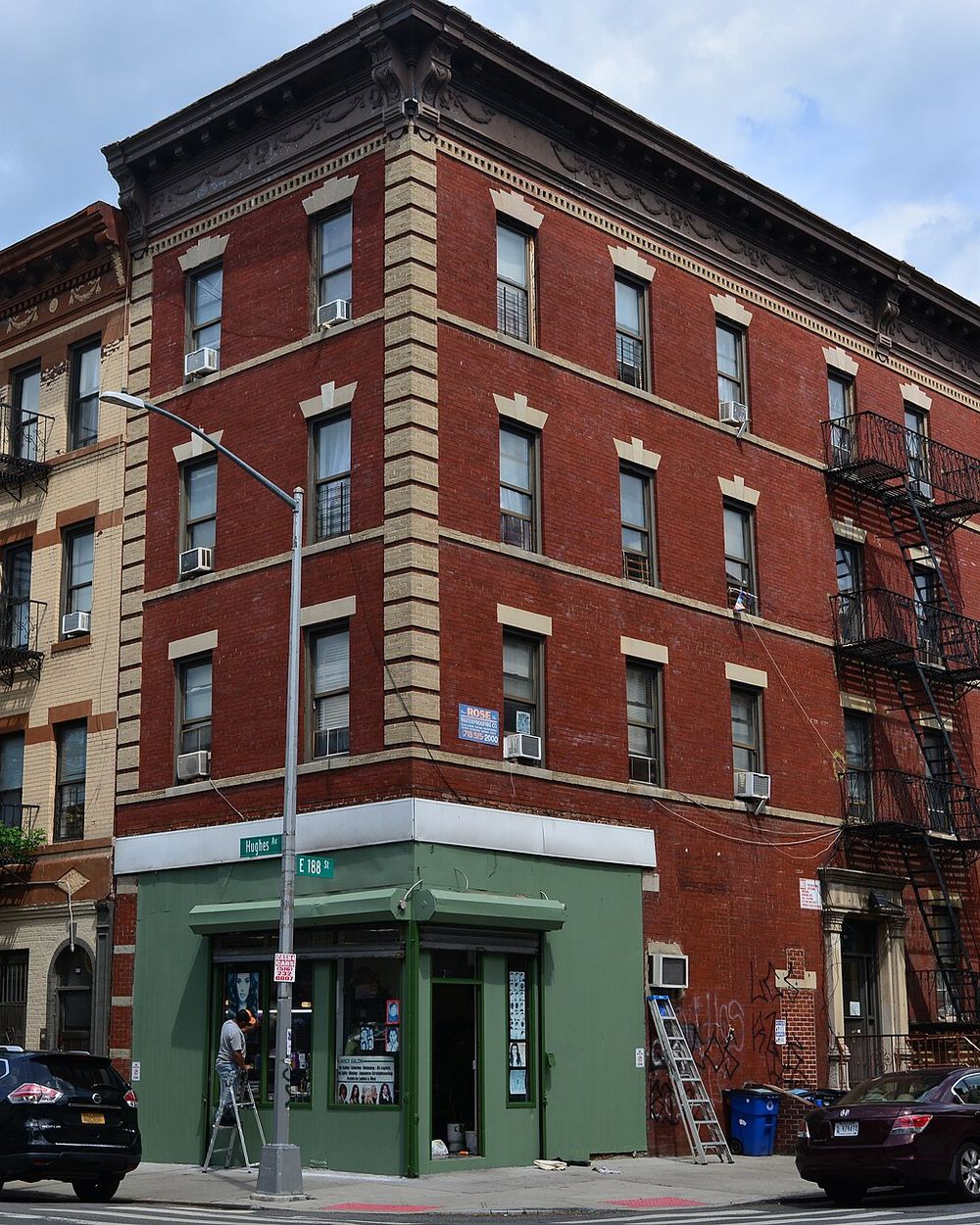 Red brick walk-up apartment building with fire escapes on a corner in Belmont, the Bronx